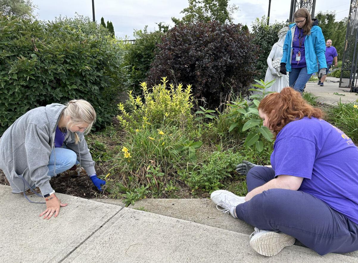 Two female students work in a plant bed in Eldridge Park